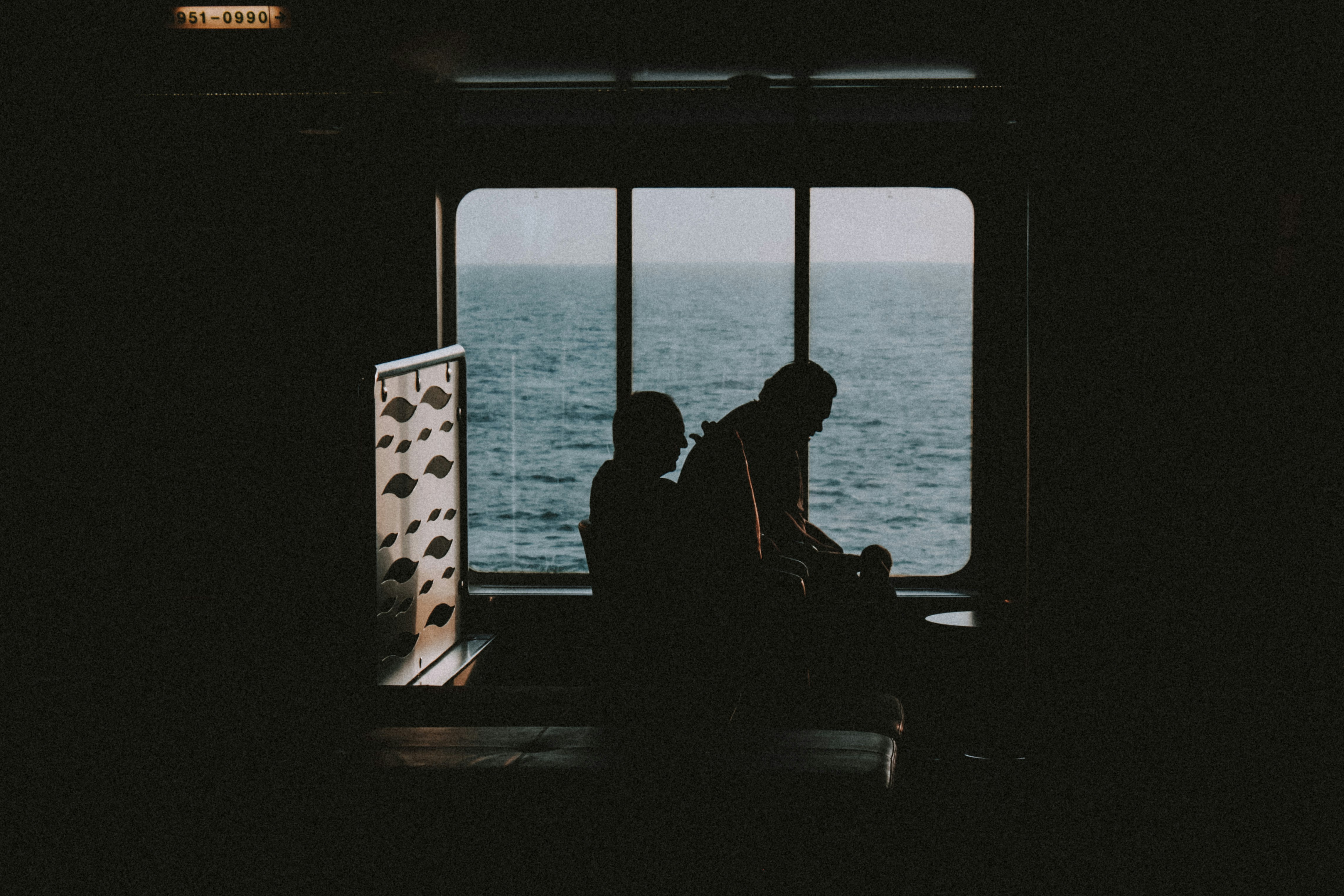 silhouette of 2 people sitting on chair in front of sea during daytime